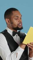 Vertical Hotel concierge in tuxedo reading a novel story book in studio, enjoying literature and lecture hobby. Hospitality industry staff working in five star lodging resort, bellhop receptionist. Camera A. video
