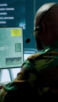 Vertical Military personnel in a base of operations using advanced computers and big screen, monitoring satellite systems to enhance security measures and process data. High tech army gear. Camera A. video