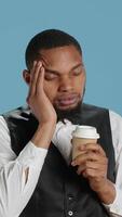 Vertical Unwell hotel porter feeling sick and drinking a cup of coffee, dealing with a migraine and flu symptoms while on duty. Receptionist bellhop staff works with a headache. Camera A. video