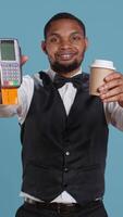 Vertical Hotel porter showing the pos terminal with card to symbolize electronic transaction at front desk. Bellboy with uniform receives payment for the lodging and amenities at the resort. Camera B. video