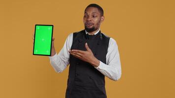 Waiter showing a tablet with isolated copy space in studio, working in a service oriented environment and catering industry. Friendly restaurant staff serving clients at their tables. Camera B. video