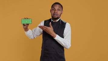 Waiter with professionalism holding a phone with isolated mockup display, working in dining and eatery industry. Friendly restaurant staff does customer oriented activity at his job. Camera B. video