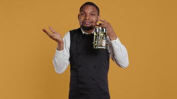 Waiter shrugging while he carries a cruet set with condiments, acting uncertain and showing i dont know symbol in studio. Professional customer focused staff is confused and unsure. Camera B. video