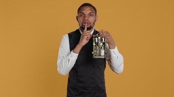 Catering staff waiter doing a mute sign for silence and privacy, keeping quiet while he carries cruet set with condiments for customer satisfaction. Shows a hush symbol to keep secret. Camera B. video