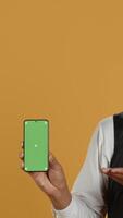 Vertical Restaurant staff showing a smartphone with green screen in studio, prepared to serve food orders in service oriented environment. Waiter with apron and uniform serving clients at tables. Camera A. video