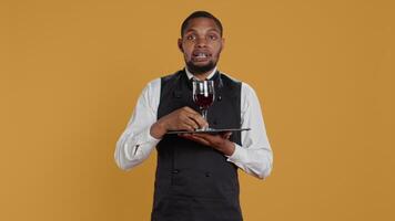 Waiter serving clients with a glass of red wine before dinner, recommending a special drink for customer satisfaction. Employee carrying a tray and serves people with professionalism. Camera B. video