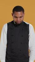 Vertical Portrait of restaurant waiter wearing professional uniform and apron getting ready to assist and serve clients. Employee working in service oriented environment for customer satisfaction. Camera B. video