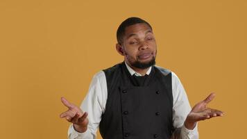 Professional waiter showing clueless sign and being unsure, shrugging and saying i dont know in studio. Confused butler staff in apron feeling uncertain and doubtful about something. Camera A. video