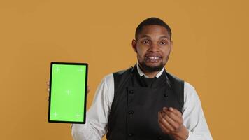 Waiter showing a tablet with isolated copy space in studio, working in a service oriented environment and catering industry. Friendly restaurant staff serving clients at their tables. Camera A. video