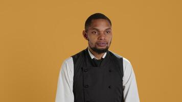 Waiter flexing his muscles and showing his strength in studio, acting tough while he wears his restaurant uniform and apron. Professional employee in service oriented industry. Camera A. video