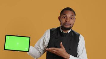 Catering employee presenting an isolated chroma key display while he wears an apron and serving clients at diner. Hospitality industry staff in professional attire, customer satisfaction. Camera A. video