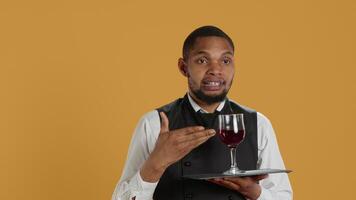 Waiter serving clients with a glass of red wine before dinner, recommending a special drink for customer satisfaction. Employee carrying a tray and serves people with professionalism. Camera A. video
