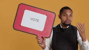 Professional waiter showing a message to vote on speech bubble, creating an advertisement for politics on cardboard icon. Restaurant employee working in customer oriented industry. Camera A. video