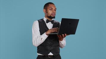 Bellhop employee making online remote reservations on laptop, browsing the hotel website to check lodging and availability. Doorkeeper staff gives assistance to guests. Camera B. video