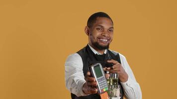 Skilled restaurant employee waiter presenting electronic payment method, showing the pos terminal with a card in it. Confident catering staff working in a customer focused environment. Camera A. video