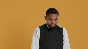 Portrait of restaurant waiter wearing professional uniform and apron getting ready to assist and serve clients. Employee working in service oriented environment for customer satisfaction. Camera A. video