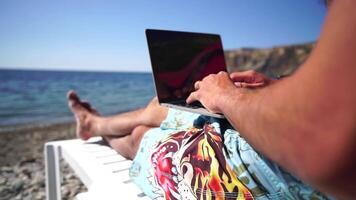 Man laptop sea. Working remotely on seashore. Happy successful man, male freelancer working on laptop on beach, relieves stress from work to restore life balance. Freelance, remote work on vacation video