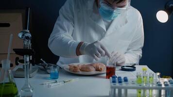 Scientist from food testing laboratory tests food for infection, chemical and Genetically Modified Organisms GMO by applying a red liquid with a pipette to chicken breast for chemical reactions. video