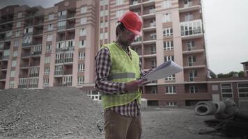 construtor lendo plantas em construção local. debaixo construção. profissional engenheiro arquiteto dentro protetora trabalhos roupas pensativamente examina plano para a construção do residencial área. video