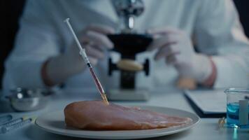 Food quality control concept. Lab assistant testing GMO chicken. Scientist examining sample meat, syringes with anabolic and antibiotics, microscope in laboratory. Food bio engineering process. video