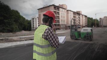 Working process. Contractor in working uniform control according to plan. Builder phone call and walking along construction site of new residential area. Foremant supervising construction. video