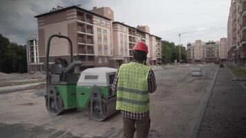 Builder in protective work clothing walks through construction of houses talking on phone with cbuilding plan of objects in hands. Foreman controls construction process while walking through project. video