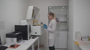 Lab technician in uniform places blood samples into automated robotic machine for analysis of biological fluids, clinical chemistry analyzer for examination of samples, medical laboratory equipment. video