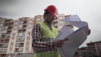 Builder reading blueprints on construction site. Under construction. Professional engineer architect in protective work clothing thoughtfully examines plan for the construction of residential area. video