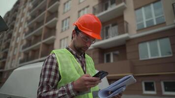 Inspection of civil construction at build site of high rise apartment house. Engineer examines documentation, plan and building progress on drawings in front of machine. Worker against of a paver. video