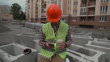 Construction worker resting on building site drinking coffee to go and using smartphone while sitting on jobsite. Architect chatting and using smartphone during coffee break at work project location. video