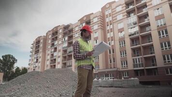 construtor lendo plantas em construção local. debaixo construção. profissional engenheiro arquiteto dentro protetora trabalhos roupas pensativamente examina plano para a construção do residencial área. video