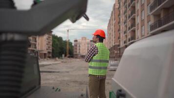 Confident engineer building architect in hard hat stands outside with his back to camera at construction site. Man foreman in helmet and safety vest standing back and looking ahead at the worksite. video