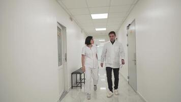 Two doctors man and woman, walk quickly down hospital corridor and discuss an MRI scan of patient. Medical teamwork. Medical workers discussing CT scan of brain and go through hallway of clinic. video