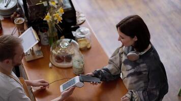 Top view close up of a brunette girl in a gray sweater paying for an order at the counter using a terminal in a cafe video