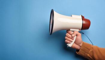 Hand Holding a Megaphone Against a Blank Blue Background photo