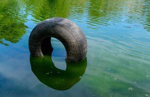 Car tire in water, Green lake reflecting the trees on its bank on a sunny day photo