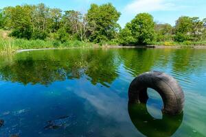Car tire in water, Green lake reflecting the trees on its bank on a sunny day photo