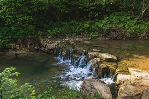 A small waterfall with rocks in the river and grass and forest in the background photo