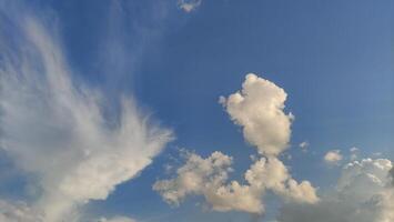 Clouds of various shapes and sizes drift across a bright blue sky photo