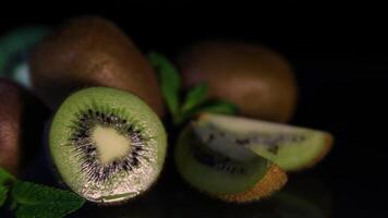 Fruits of juicy kiwi and mint leaves lie on a table on a black background. Close-up video