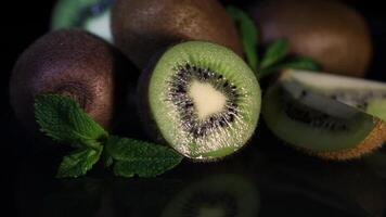 Fruits of juicy kiwi and mint leaves rotate on a table on a black background. HD. Close-up video