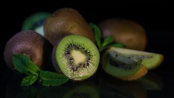 Delicious beautiful fruit kiwi and mint petals lie on a black table. Kiwi is reflected from the table video