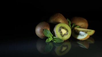 Delicious beautiful juicy kiwi fruits and peppermint petals beautifully revolve on a black table. Kiwi reflects off the table. Pieces of kiwi. HD video