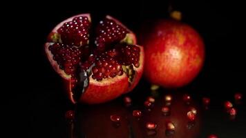 Two ripe fruit pomegranate lie on a black table on a black background video