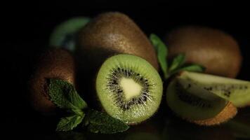 Delicious beautiful juicy fruit kiwi and mint petals lie on a black table. Kiwi reflects off the table. Pieces of kiwi video