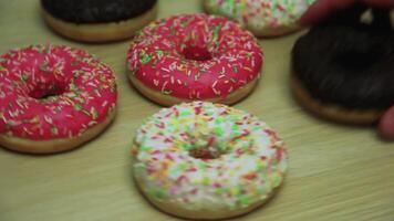 muchos rosquillas en esmaltes de diferente colores girar en un ligero de madera mesa mientras ellos son tomado lejos por mano. de cerca video