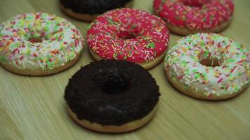 muchos rosquillas en esmaltes de diferente colores girar en un ligero de madera mesa mientras ellos son desmantelado por manos video