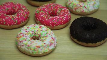 muchos rosquillas en esmaltes de diferente colores girar en un ligero de madera mesa video