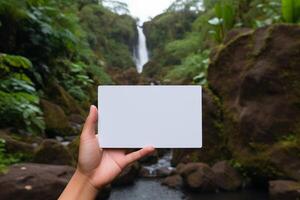 A person standing in front of a waterfall, holding a card in their hand. photo