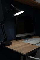 The computer desk is illuminated by a desk lamp in a dark room. Home office. The concept of working from home during overtime hours. photo